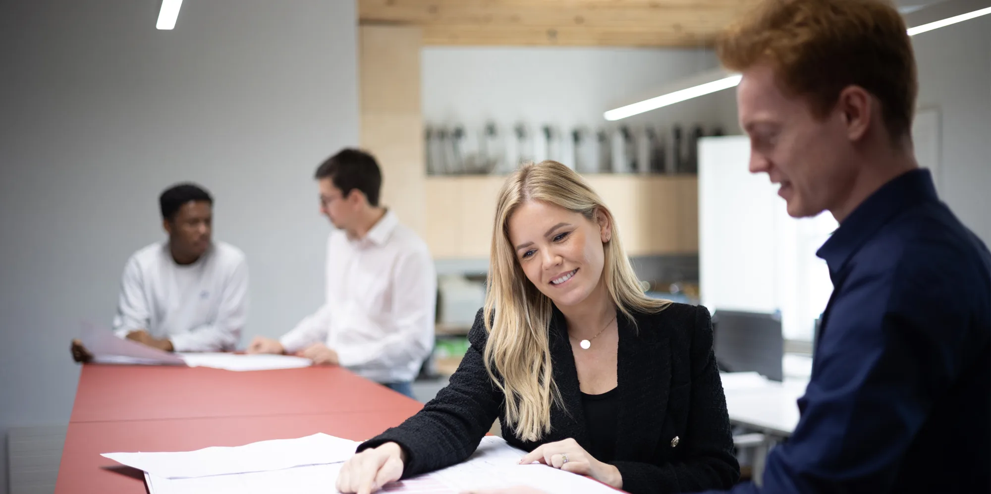 2 pairs of people discussing printed documents, one pair in the background is sightly blurred and the other is closer and in focus