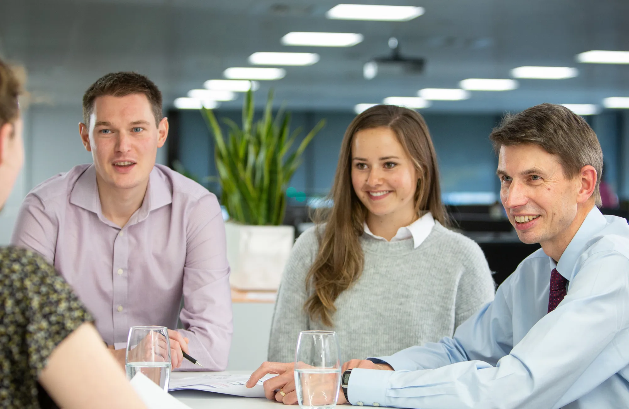 3 people talking to a fourth person with their back to the camera, against an open plan office background