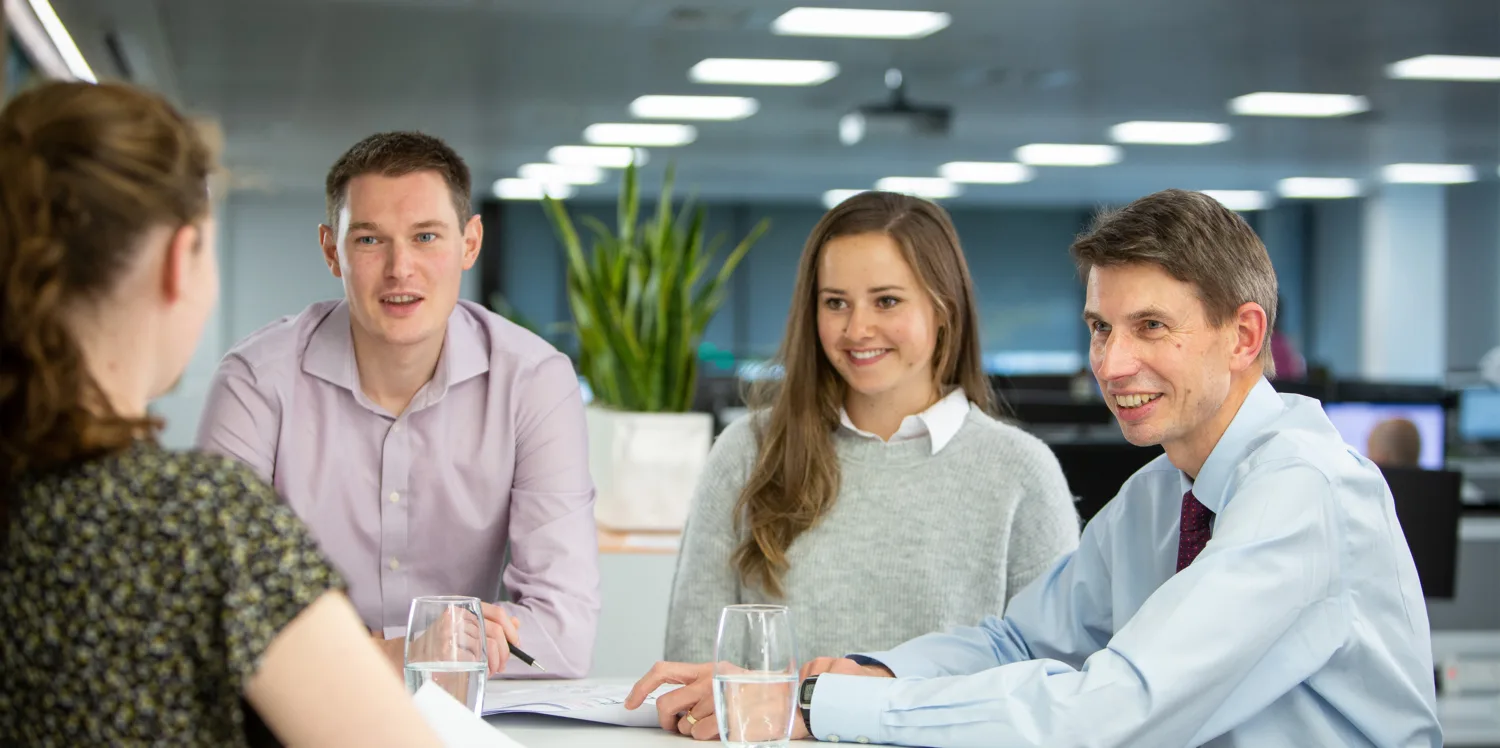3 people talking to a fourth person with their back to the camera, against an open plan office background