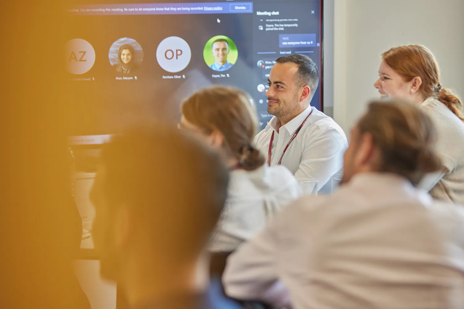 A room full of graduates watching a presentation in front of a teams screen