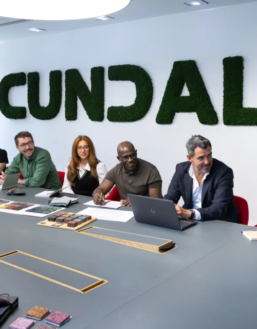 People seated around a large meeting table beneath a moss-covered Cundall wall sign, with laptops, notebooks and material samples displayed in a bright office interior.