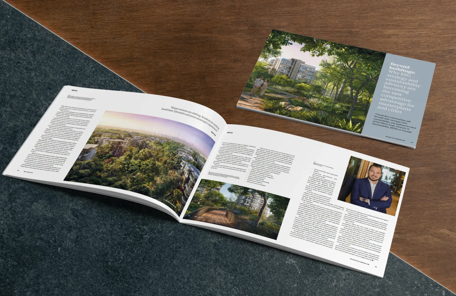 An open magazine lies on a stone and wood surface, displaying articles with images of a landscaped residential area and a walkway; visible text includes a headline page reading “Beyond buildings: Why ESG strategy and sustainability advisory are becoming the new competitive advantage for masterplans and cities.”