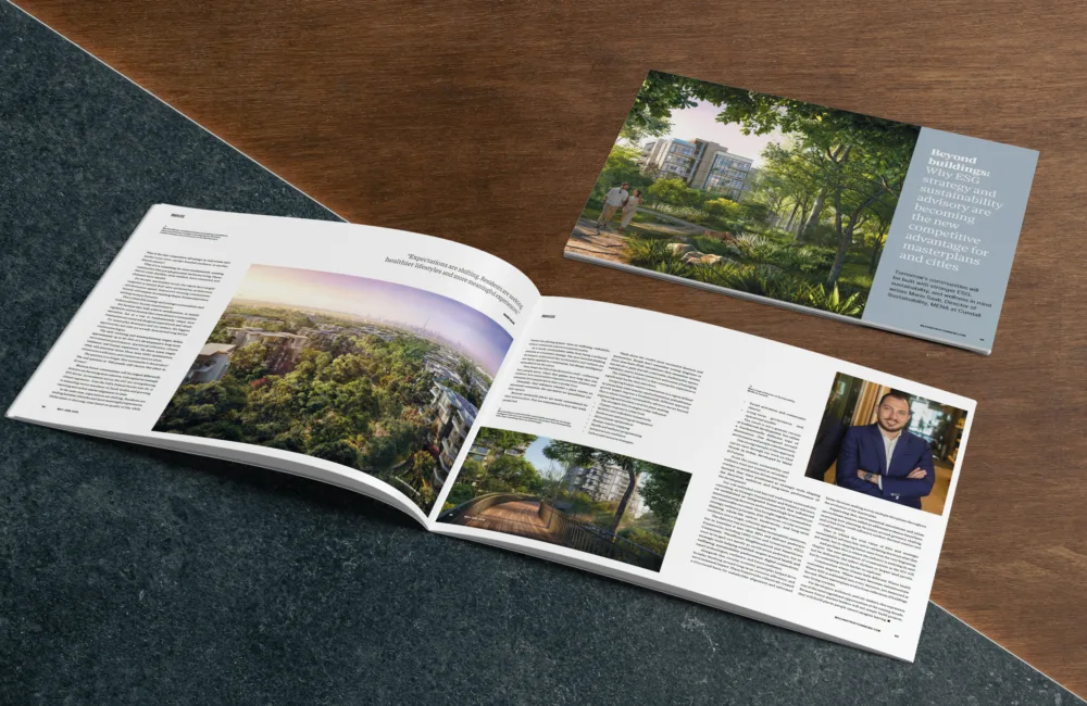 An open magazine lies on a stone and wood surface, displaying articles with images of a landscaped residential area and a walkway; visible text includes a headline page reading “Beyond buildings: Why ESG strategy and sustainability advisory are becoming the new competitive advantage for masterplans and cities.”