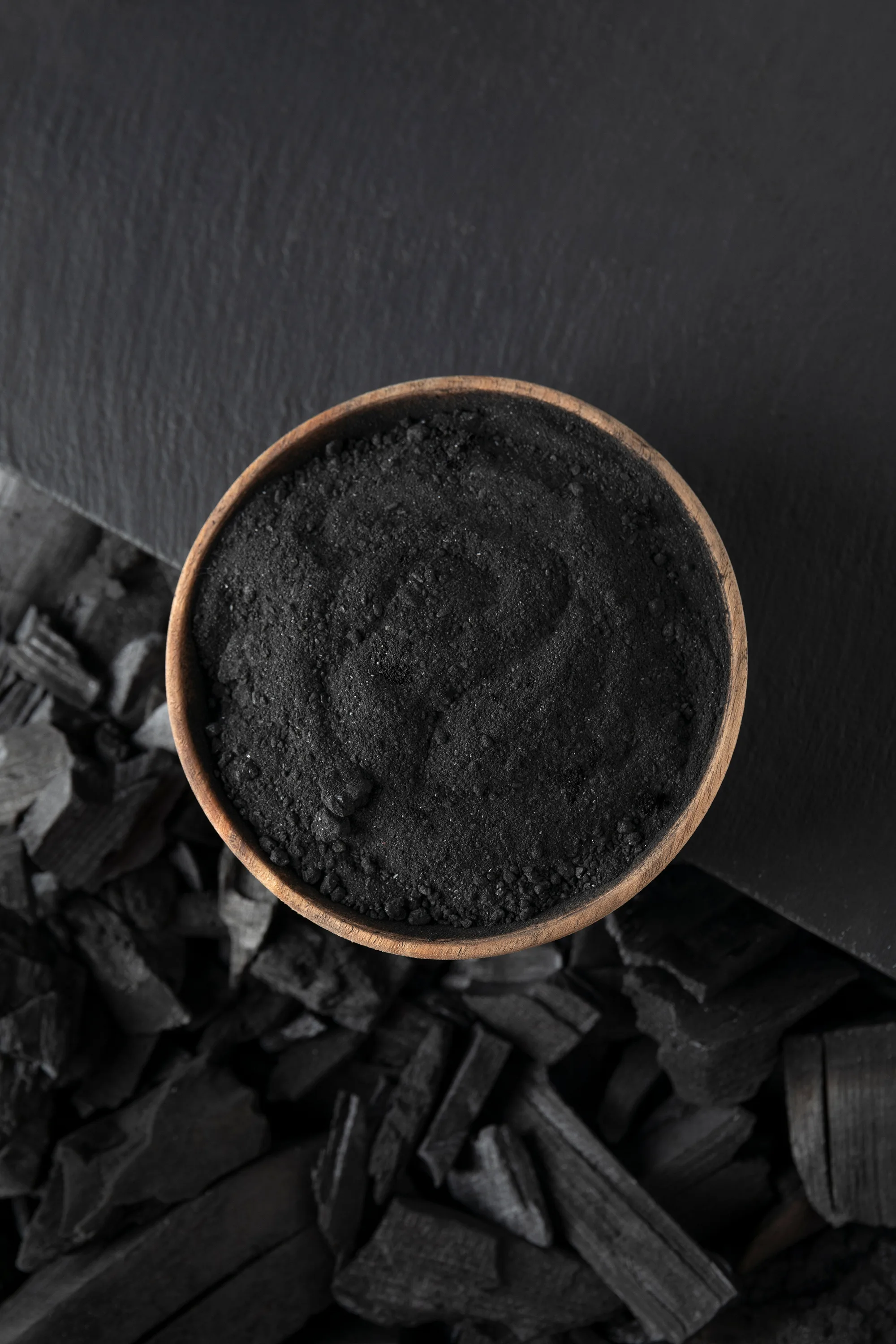 Bowl of finely ground charcoal overlapping a black table with charcoal pieces on the floor