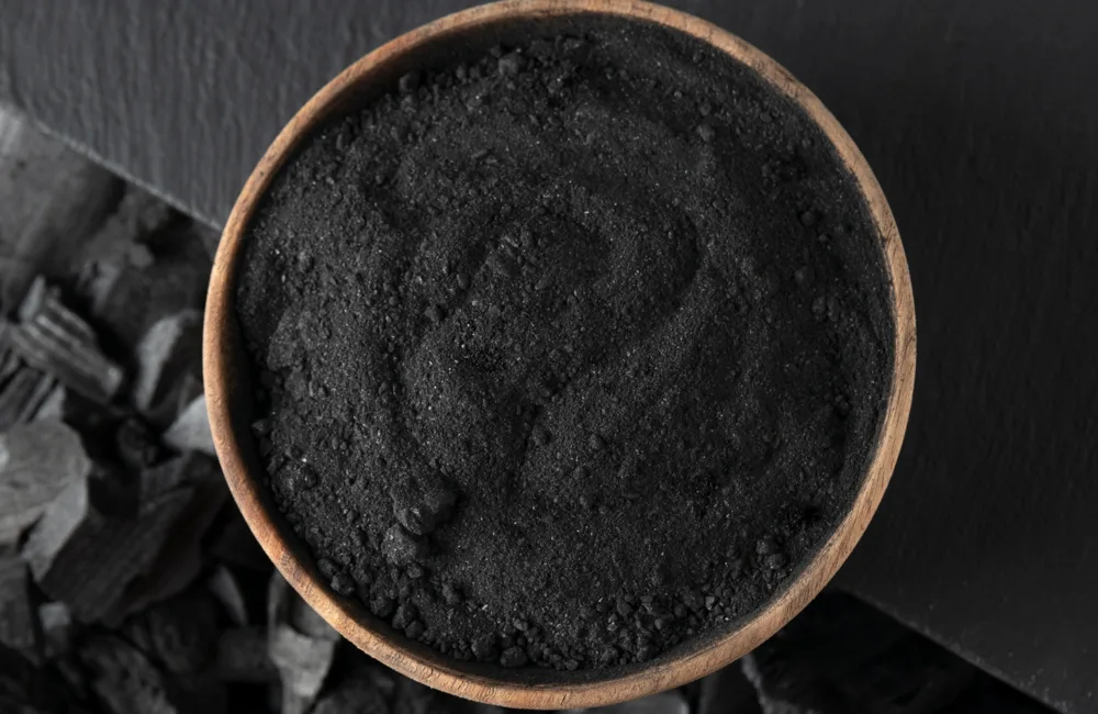 Bowl of finely ground charcoal overlapping a black table with charcoal pieces on the floor