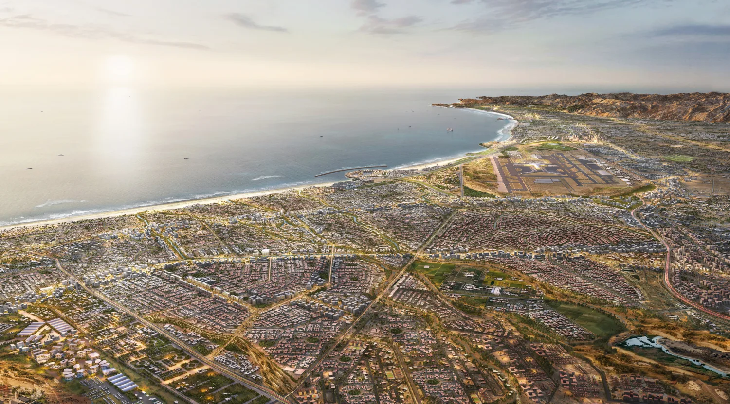 Aerial view of a coastal city with extensive residential development, road networks, shoreline, harbour structures and surrounding hills.