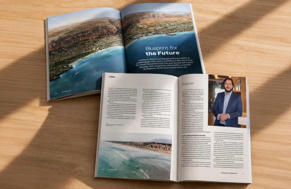 Open magazine spread on a wooden surface featuring a coastal aerial image, article pages and a portrait photograph.