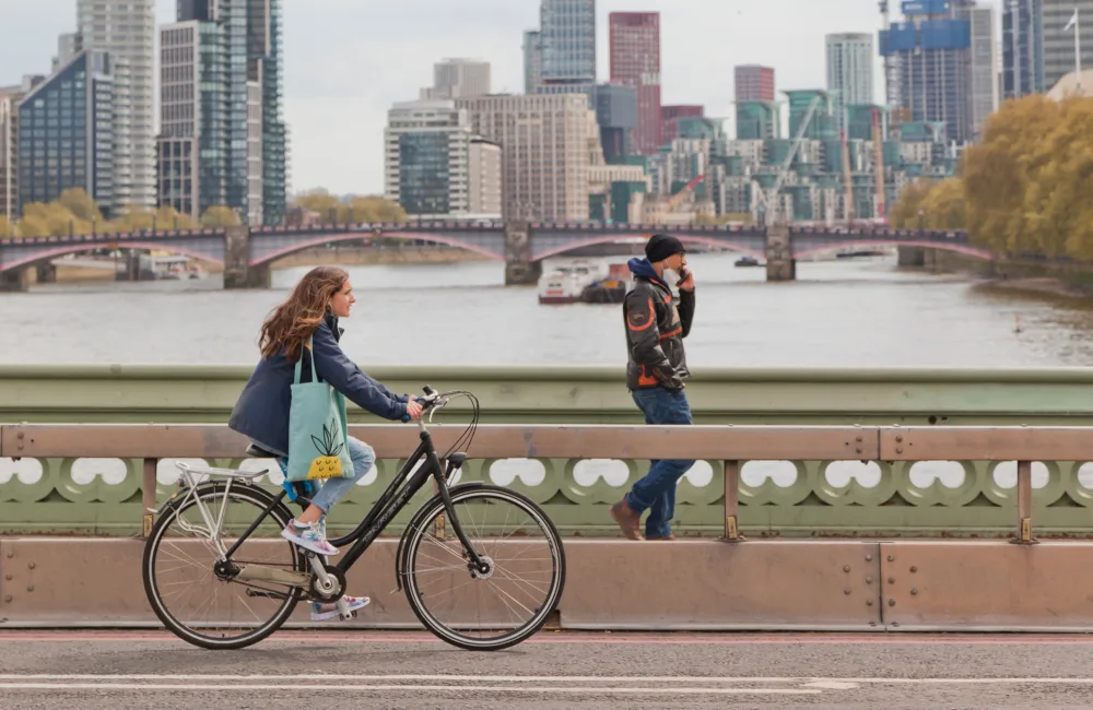 People walking and riding a bike along a bridge - buildings in background