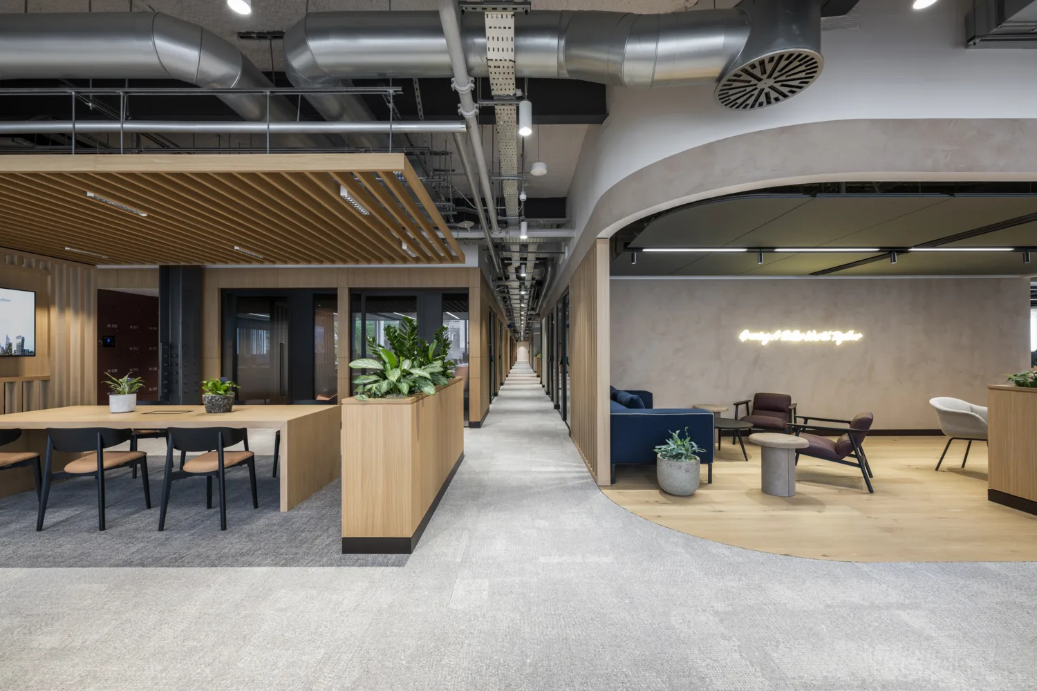 Commercial office interior with timber finishes, open seating, enclosed rooms, planting and exposed ceiling services.