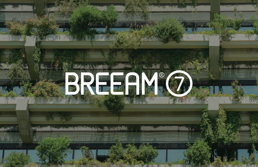 A multi‑story building façade with horizontal concrete ledges covered in dense green plants and shrubs, with large glass windows behind them. The centre text reads ‘BREEAM 7.