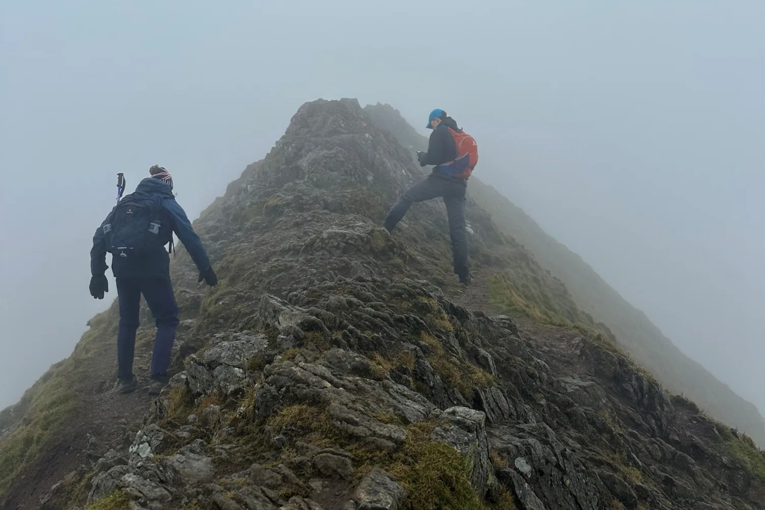 Two people climbing up the rocky mountain grey misty sky in the background