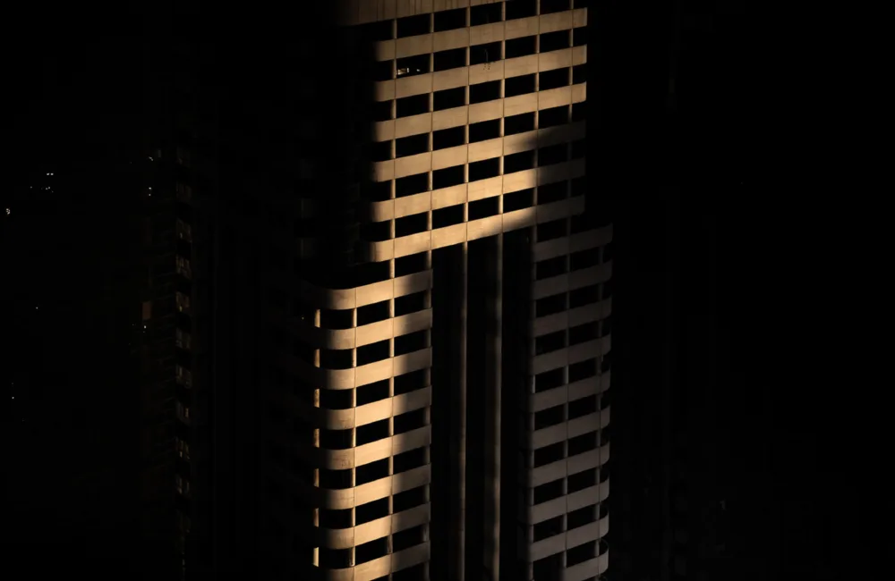 A tall building structure partially lit by light, surrounded by darkness