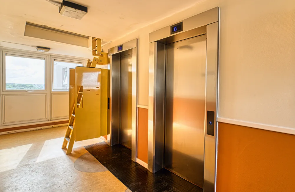 Lobby view of 2 Wigan project lifts with doors closed, and yellow ladder on the left hand side of the lifts going into the ceiling