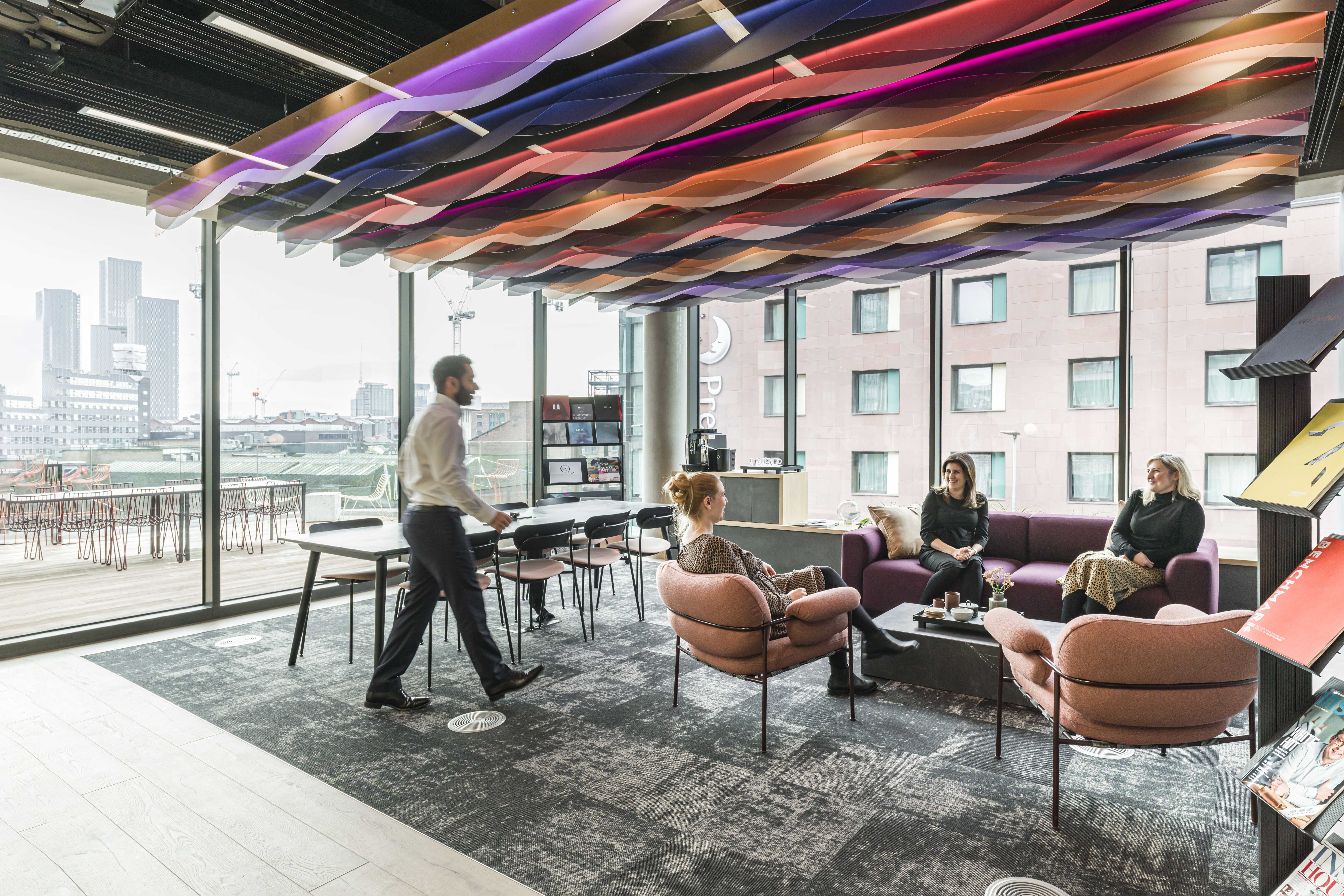 Meeting room space with people chatting on chairs, acoustic panels on ceiling and glazed window