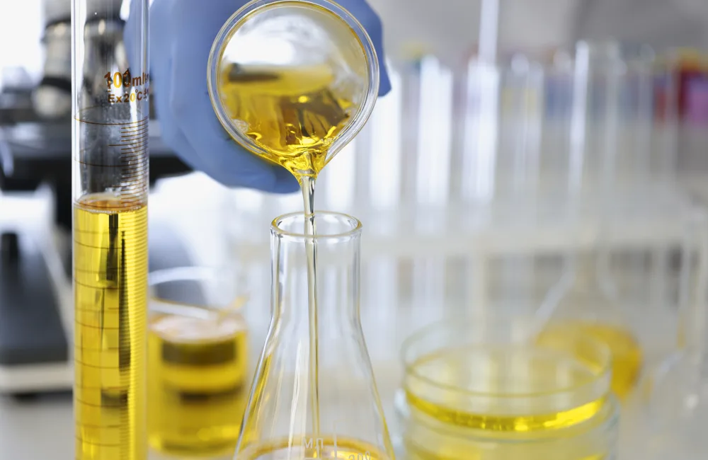 Hand in rubber glove pours yellow liquid into flask in chemical laboratory closeup. Pharmacological preparations production concept.