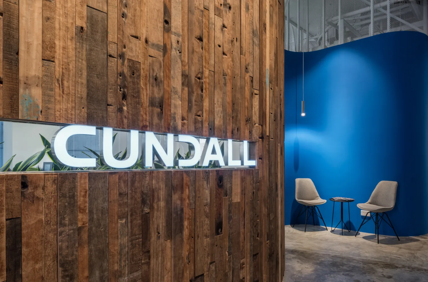 Cundall sign set into a reclaimed timber wall beside a blue curved wall with two chairs and a small table.