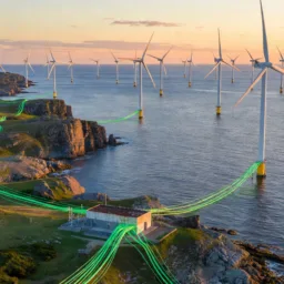 Wind turbines stand offshore in a large array, with cables highlighted in green extending from turbine bases across the sea to a rocky coastline and inland fields, connecting to a small utility building on land.