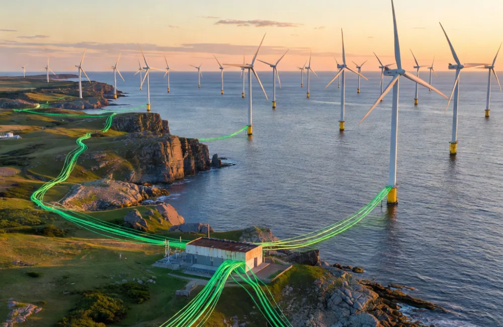Wind turbines stand offshore in a large array, with cables highlighted in green extending from turbine bases across the sea to a rocky coastline and inland fields, connecting to a small utility building on land.