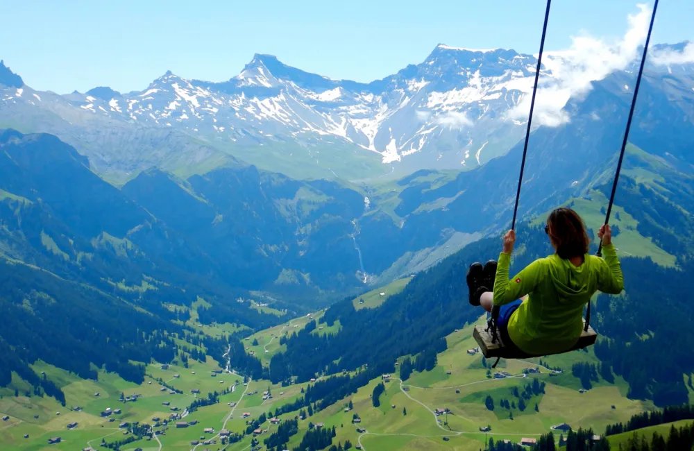 Person in green top on a swing with a mountain range backdrop