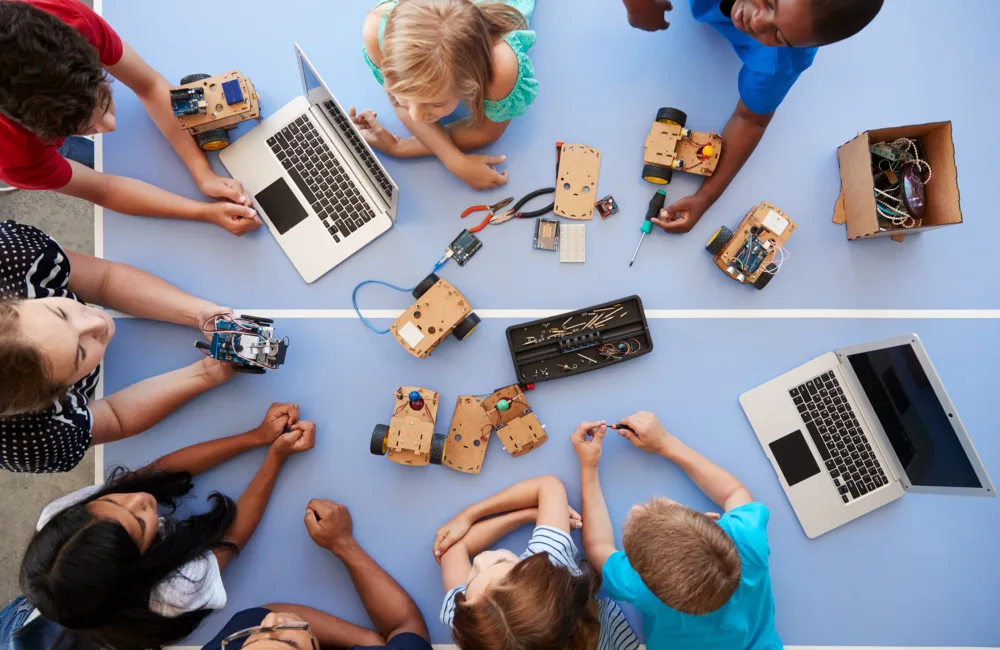 Overhead View Of Students In After School Computer Coding Class Learning To Program Robot Vehicle
