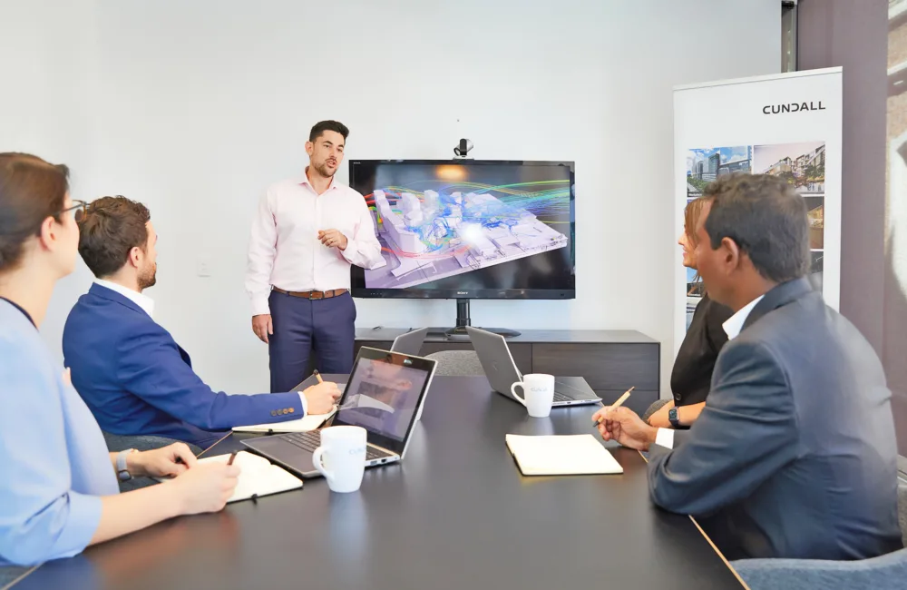 Group of Cundall people sitting around a table watching someone present in front of a TV screen