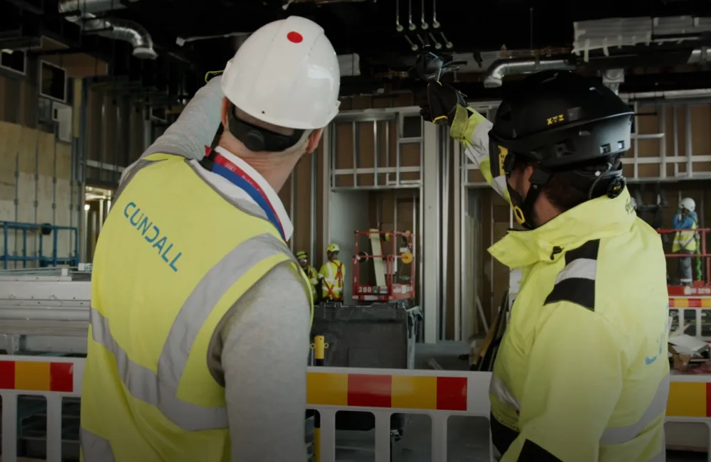 two men in high vis and hard hats talking and pointing on construction site