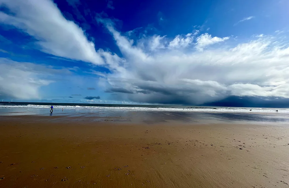 Beach with a blue sky and clouds, with people near the sea