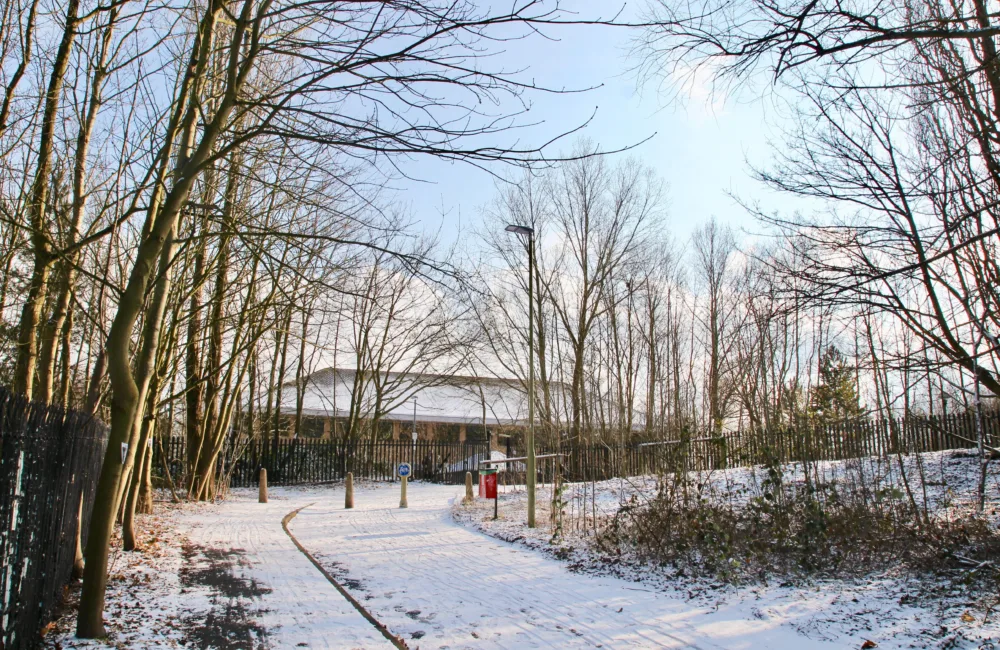 Cycle path with building in the background on a snowy winter day with a pale blue sky