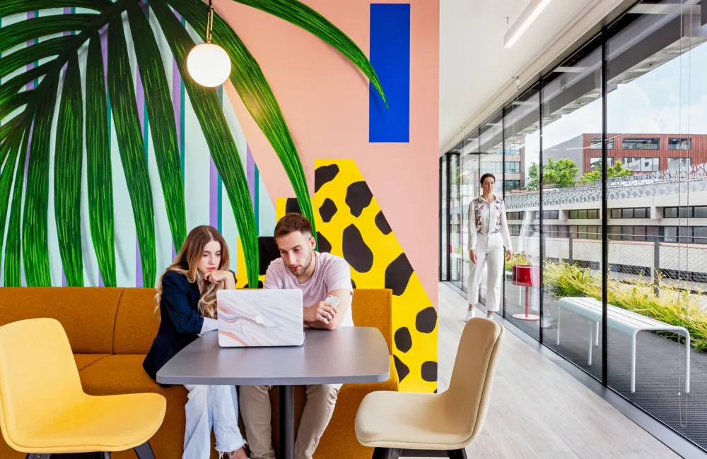 Vibrant painted wall next to a glazed corridor with people collaborating over a laptop