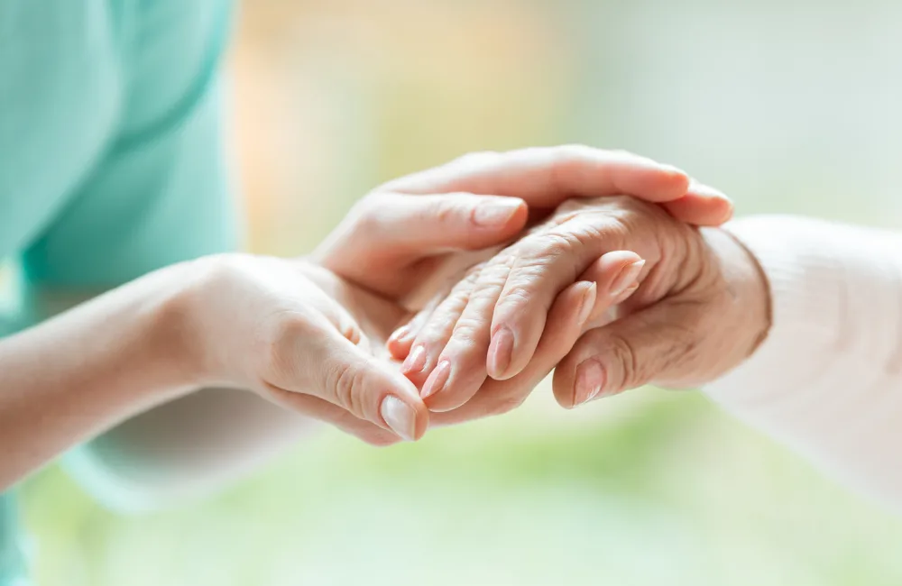 Nurse gently holding the hand of an elderly woman.