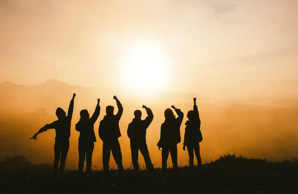 Silhouette of a group on a mountain with arms raised pumping the air
