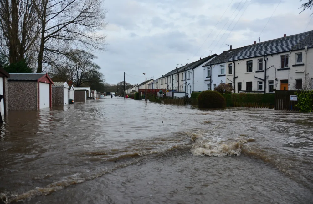 Flood street with garages and housing with people in the distance deep in water