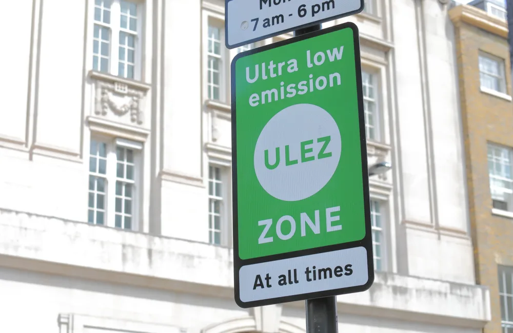 ULEZ sign in green and white with a white building in the background