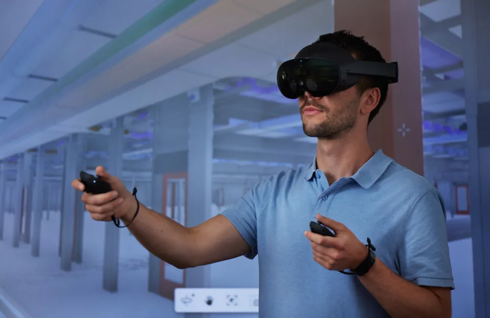 Head a sholders of man in blue shirt standing in front of screen wearing VR googles
