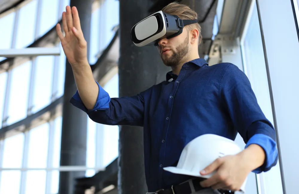 An engineer holding a hardhat and wearing a VR headset in a building.