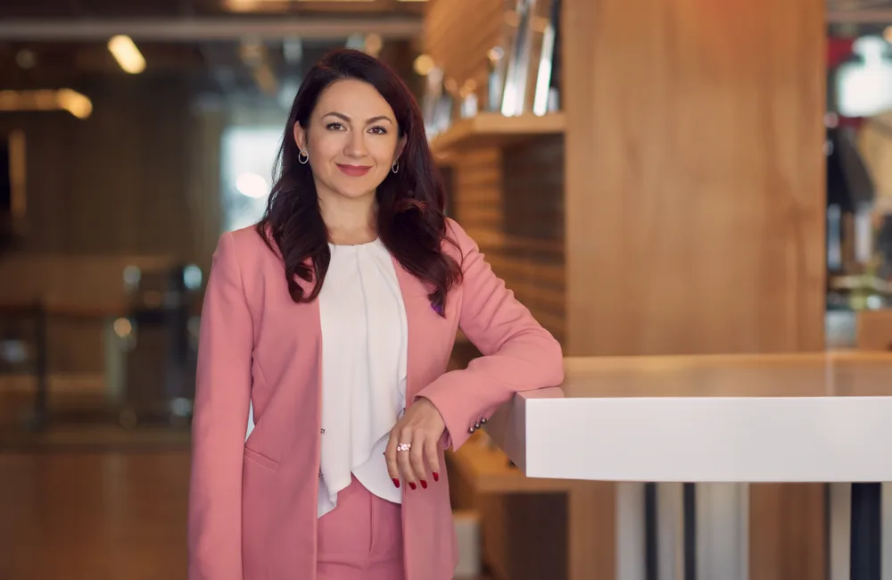 Olga Litkovets leaning in a cantilevered table in our Dubai office with her pink coat