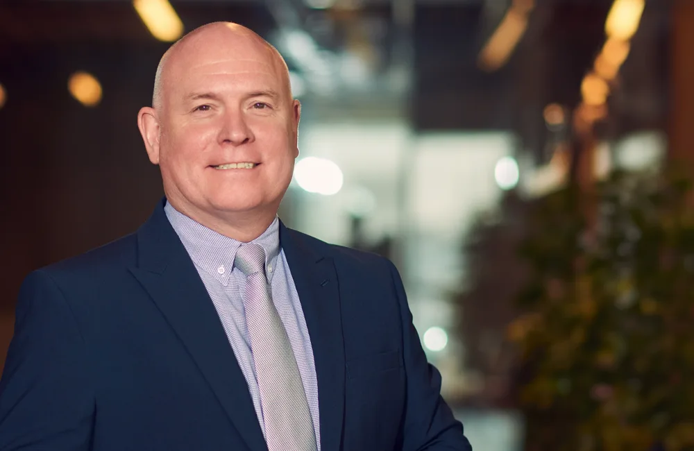 Richard Stratton smiling in-front of a camera in a photoshoot session with glass and plan on the background.