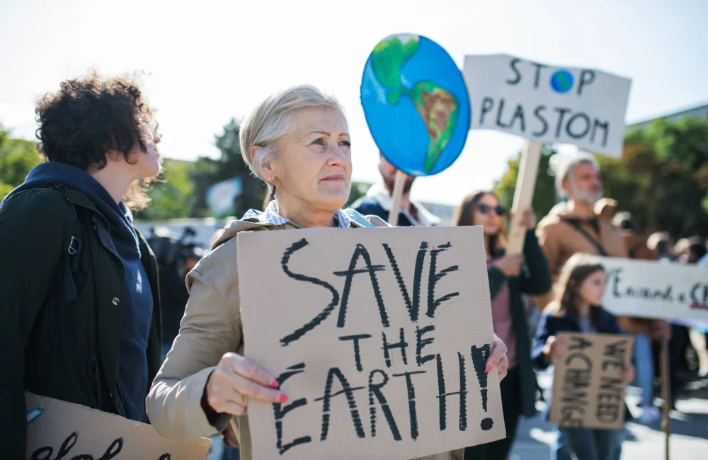 Older woman holding a sign saying 'save the earth' in a climate protest