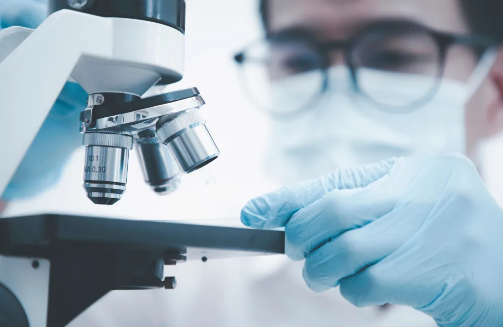 Close up of microscope with man blurred in background wearing mask