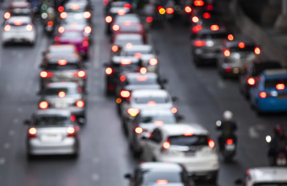 Heavy traffic on a multi‑lane road with rows of cars and motorcycles. Vehicles are closely packed, and red brake lights are visible throughout the scene.