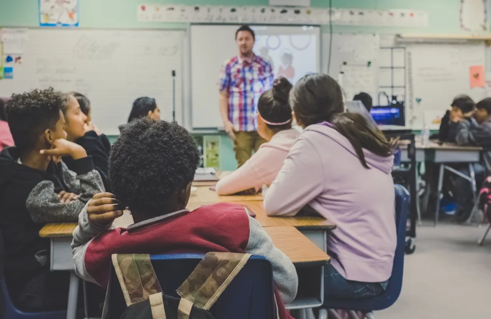 Teacher stood in front of a whiteboard in a full classroom
