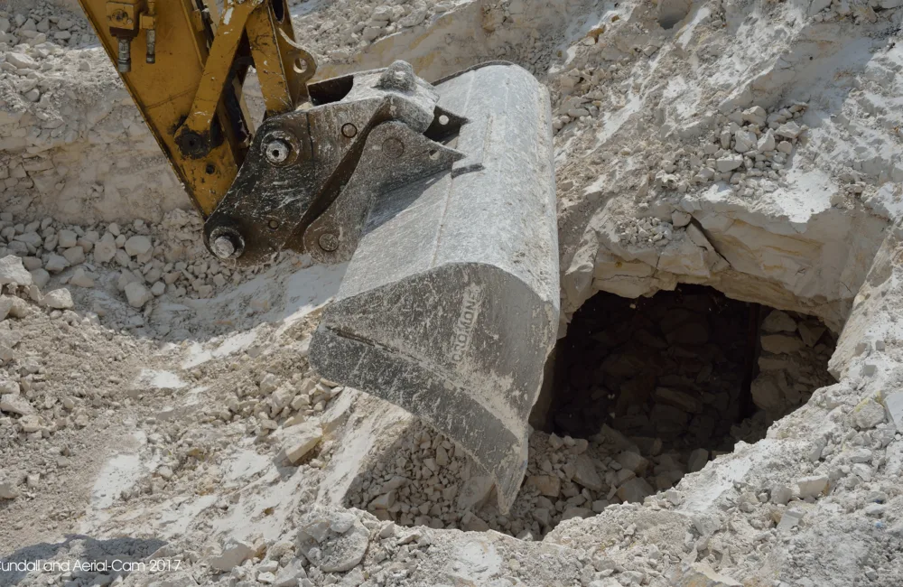 End of a digger arm making a hole in rocky soil