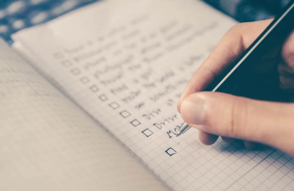 Close view of a person writing a checklist in a square papered notebook