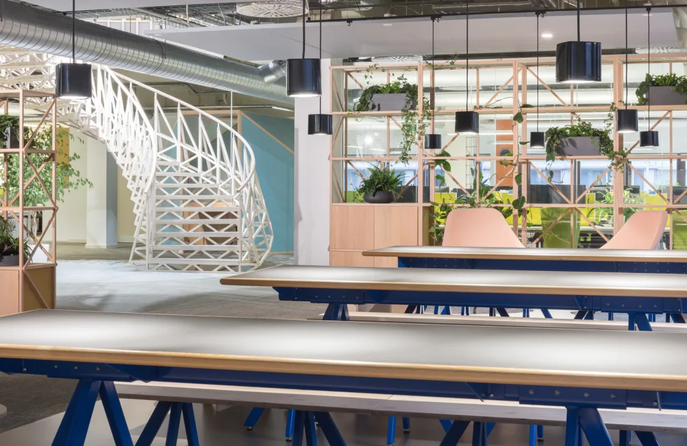 Interior of Cundall Birmingham office, white geometric staircase in background and grey and blue tables in the foreground