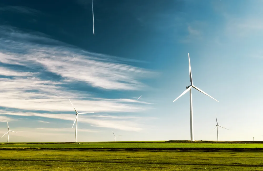 Several wind turbines standing in a green field against a deep blue sky with wispy clouds