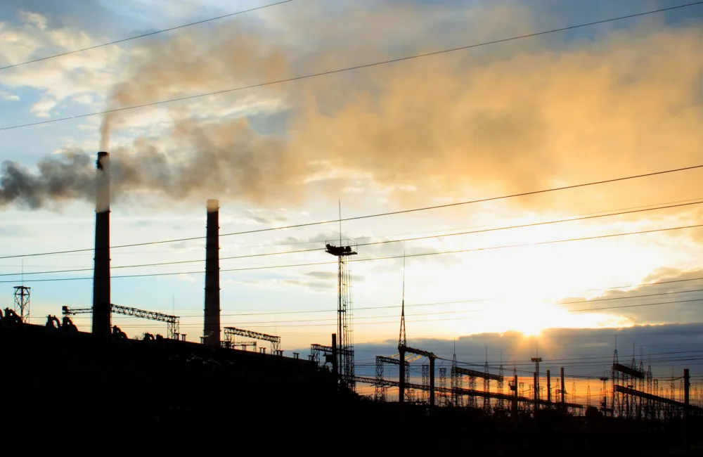 Silhouette of industrial equipment including chimneys which are producing smoke against a blue sunny sky