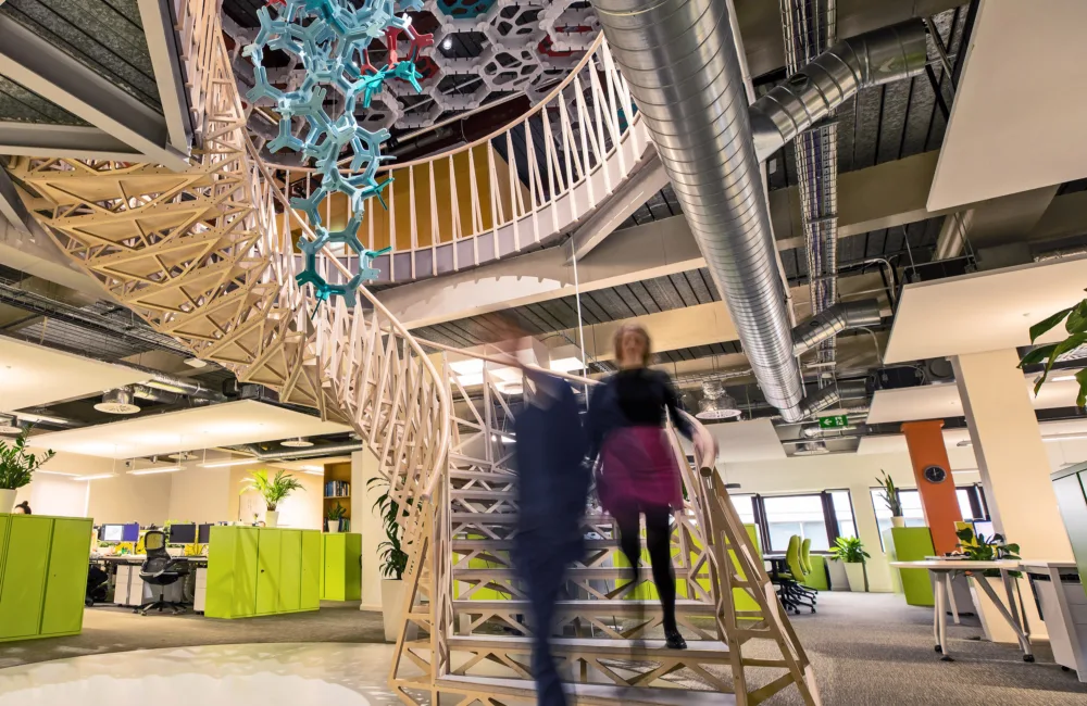 2 blurred figures walking down a central wooden spiral staircase