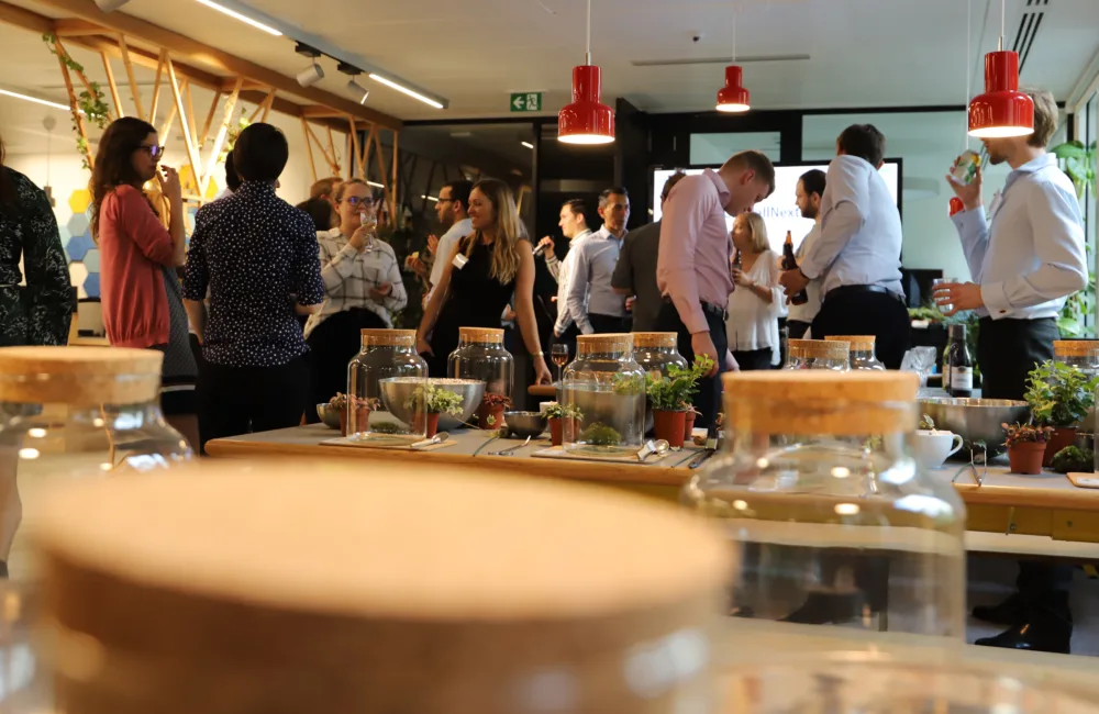 Glass jars with cork lids in the foreground and a group of people talking in the background