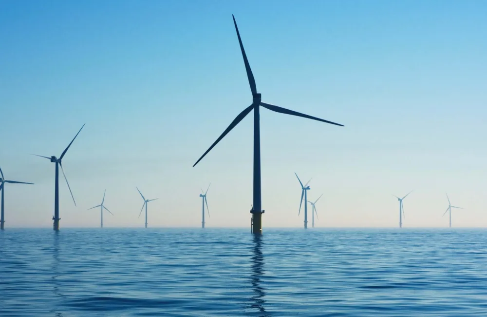 2 rows of wind turbines in a calm sea with a blue sky and boat in the back ground