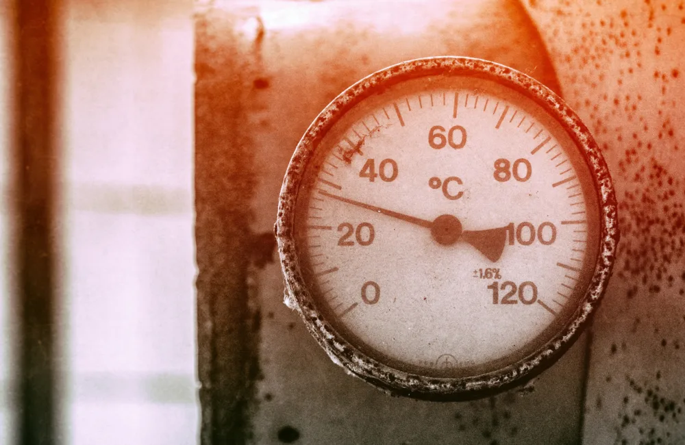 A red tinted photograph of a thermometer dial pointing at around 30 degrees Celsius